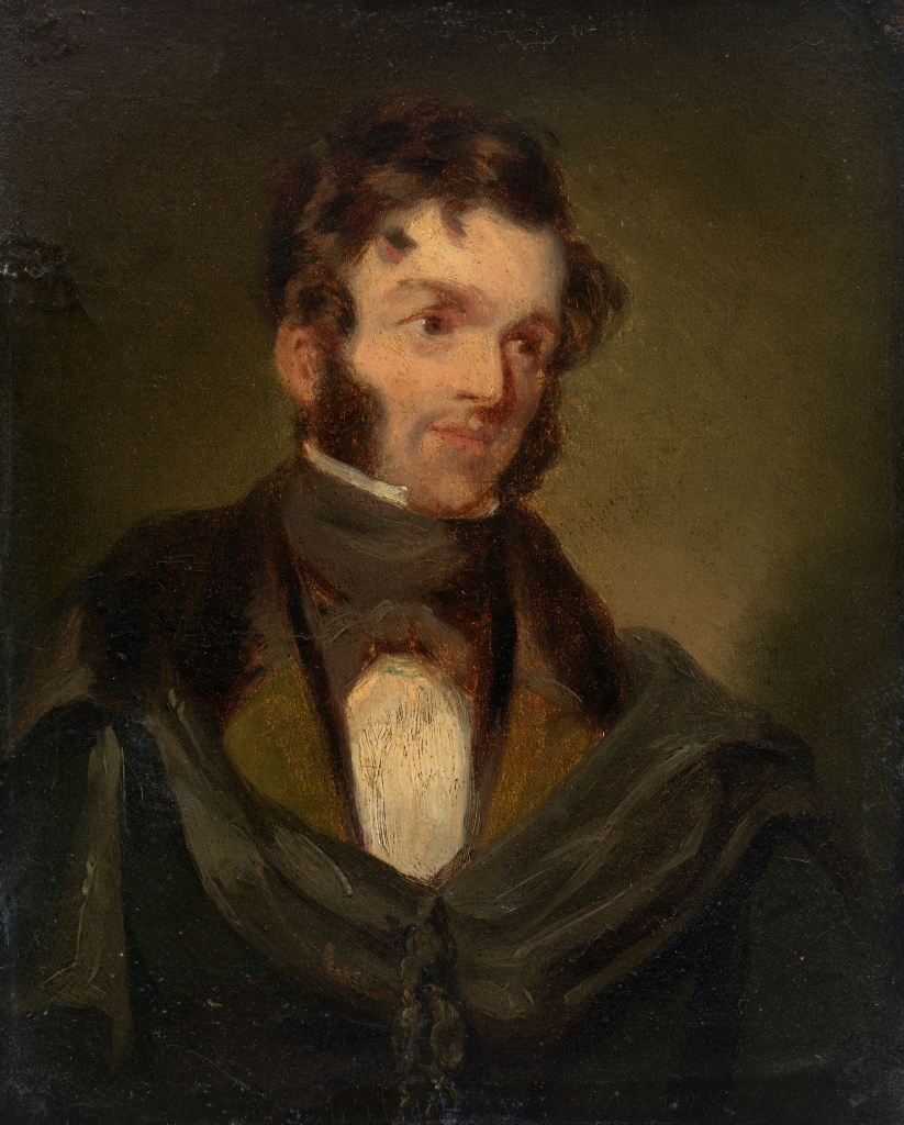 A head and shoulders portrait of a man. He has dark hair and long sideburns. He is wearing a white shirt, a brown jacket and a black cloak.